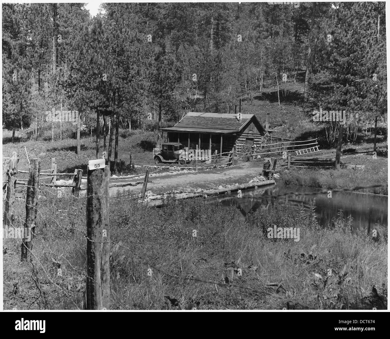 Ein Auto parkt vor einer rustikalen Hütte in Cabin Springs, mit einem ruhigen Fischteich in der Nähe, was eine ruhige ländliche Umgebung schafft. Stockfoto
