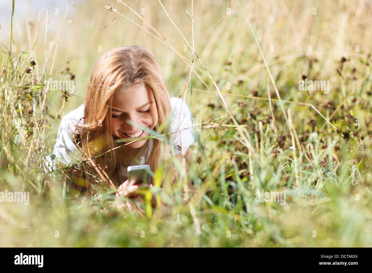 Mädchen schreibt Sms auf dem Handy im Grass liegen Stockfoto