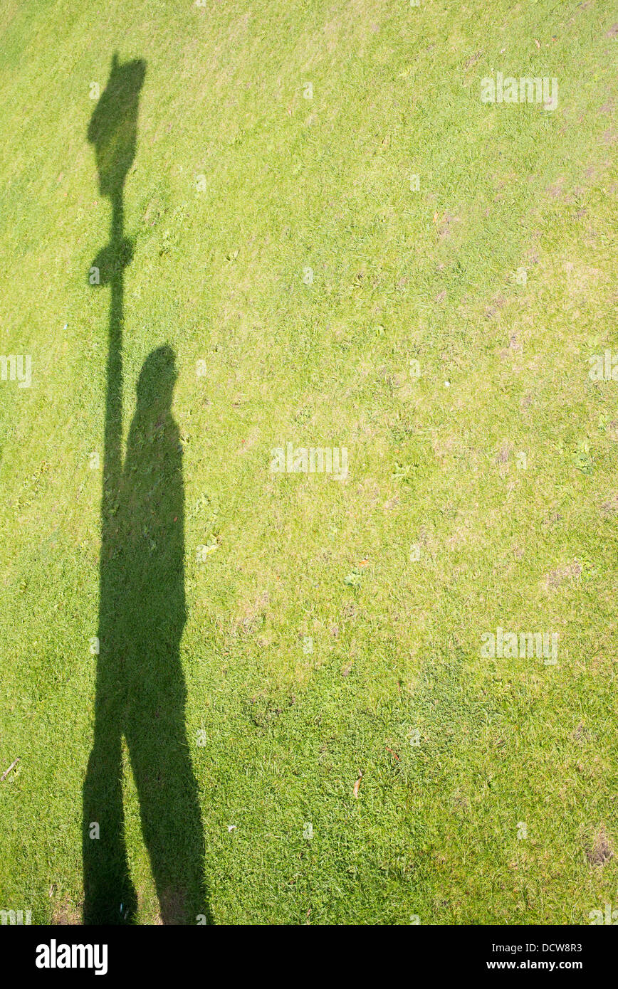 Schatten eines Mannes auf einer Wiese an einem Laternenpfahl gelehnt Stockfoto