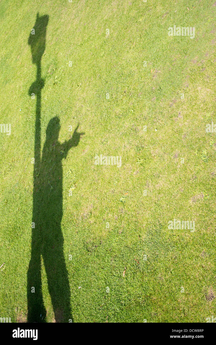 Schatten eines Mannes auf einer Wiese an einem Laternenpfahl zeigt mit seiner Hand gelehnt Stockfoto