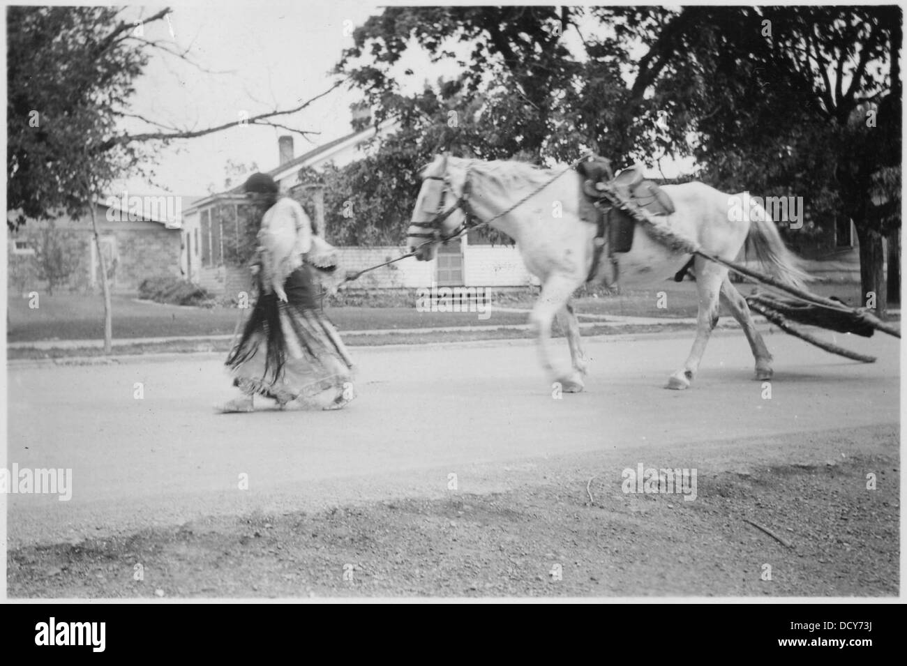 Indische Frauen, die ein Pferd führen, ziehen einen Travois durch die Straßen, eine traditionelle Transportmethode, die indigene kulturelle Praktiken hervorhebt. Stockfoto