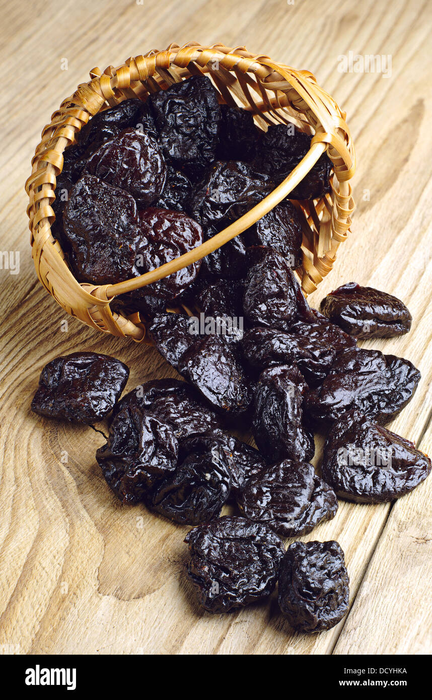 Getrocknete Pflaumen in einem Weidenkorb und in der Nähe auf einem hölzernen Hintergrund Stockfoto