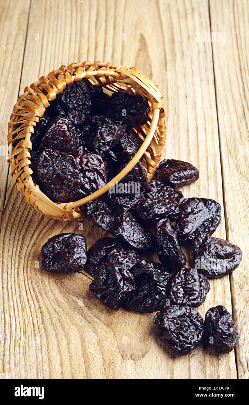 Getrocknete Pflaumen in einem Korb und verstreut auf Holztisch Stockfoto