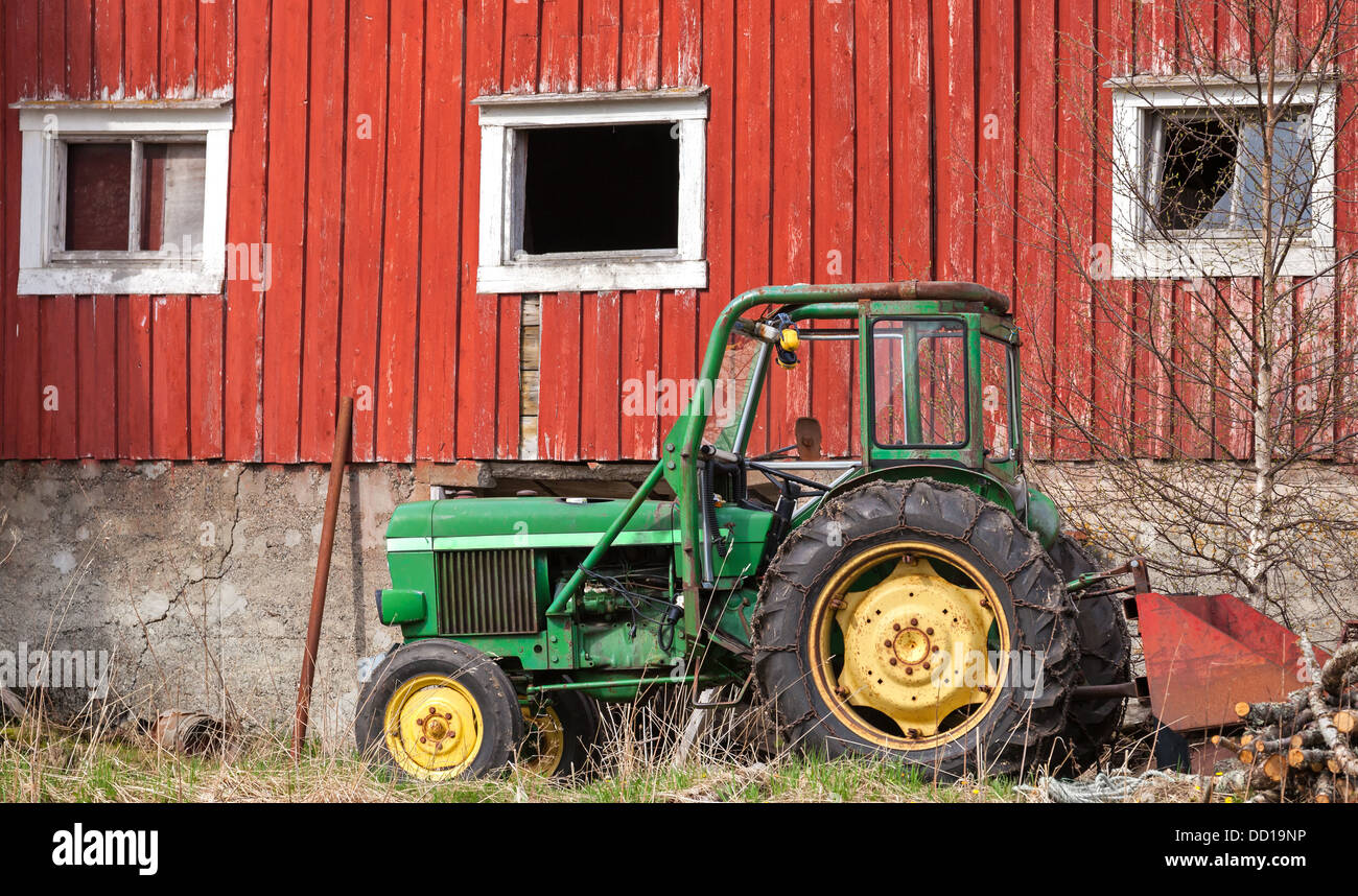 Kleiner grüner Traktor steht auf dem Rasen in der Nähe rote Scheune Wand in Norwegen Stockfoto