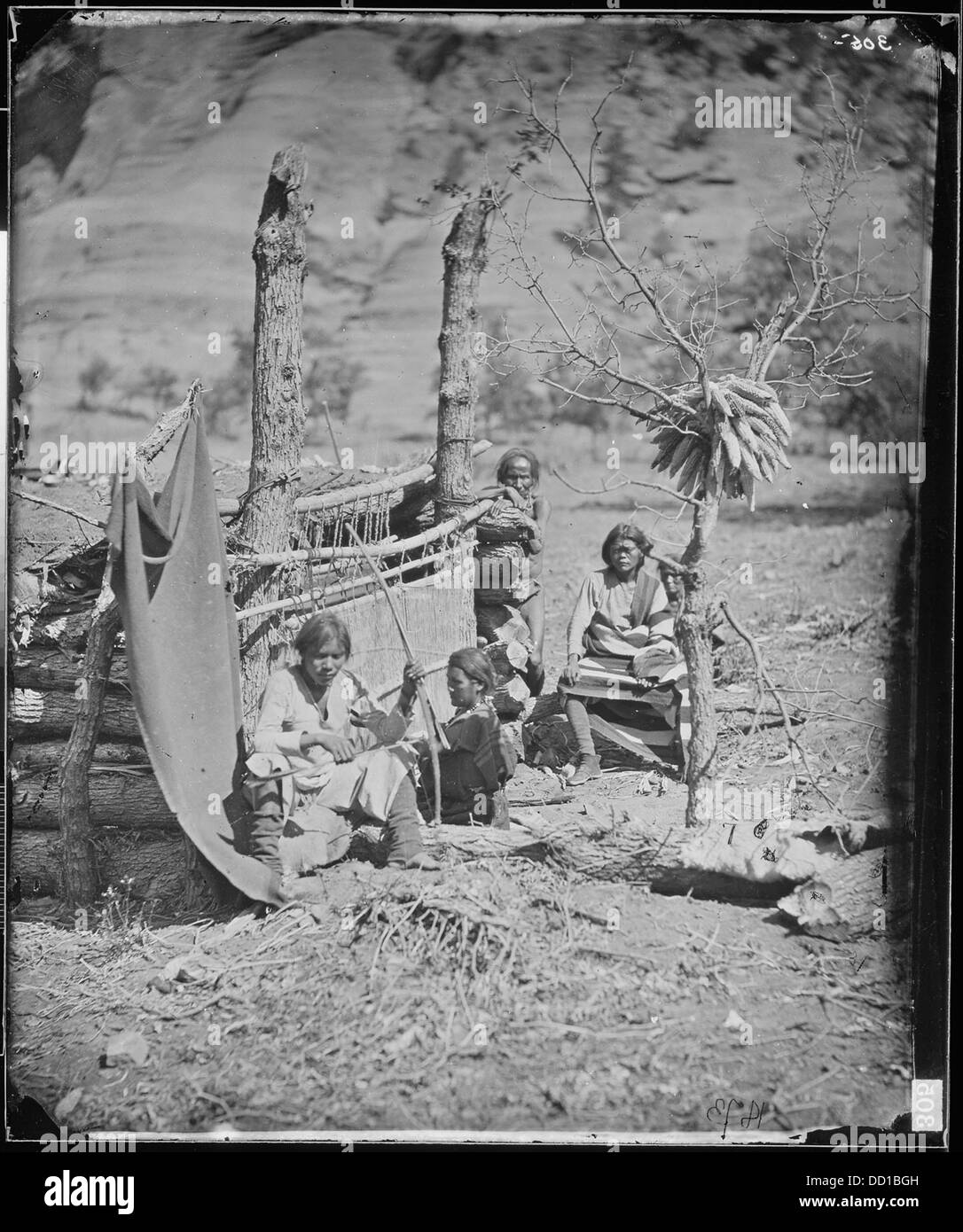 Eine Navajo-Familie im Canyon de Chelle, New Mexico Territory, mit einer Frau, die am Webstuhl webt, und einem Mann, der Bogen und Pfeil hält. Diese Szene zeigt das traditionelle Leben der Navajo im 19. Jahrhundert. Stockfoto