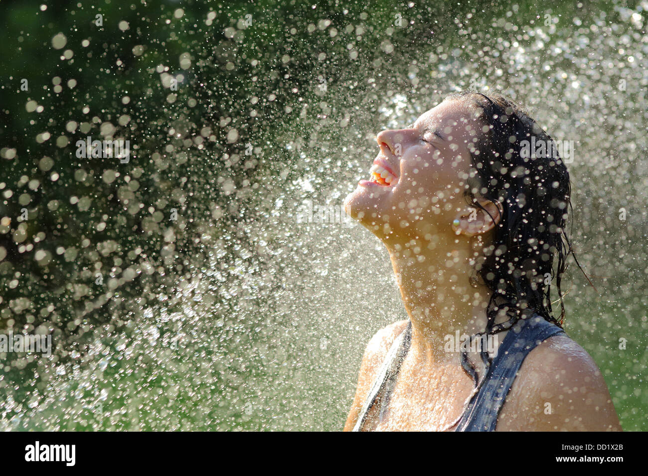 Schöne Frau, die unter einem Wasserstrahl mit Tausenden von Tropfen im Hintergrund genießen Stockfoto
