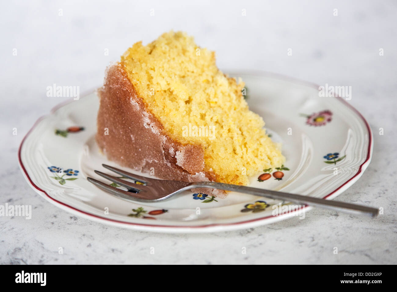Stück Heimat Zitrone beträufeln Kuchen mit Zucker Glasur oben gebacken, mit einer Blume gemusterten Teller und Kuchen Gabel Stockfoto