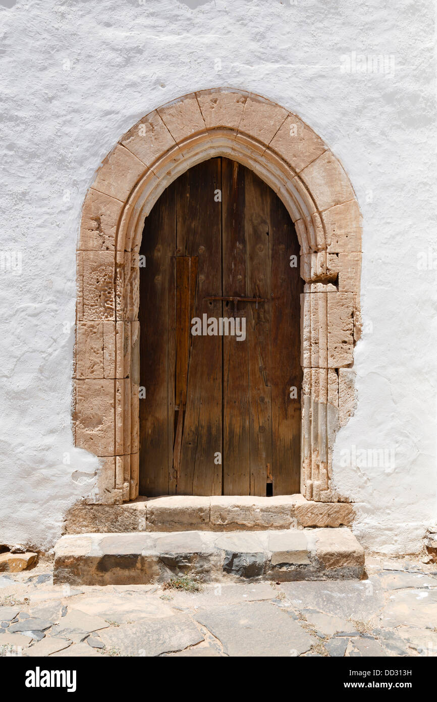 Alte hölzerne gewölbte Tür mit steinernen Torbogen und Stuck weiße Wand Stockfoto