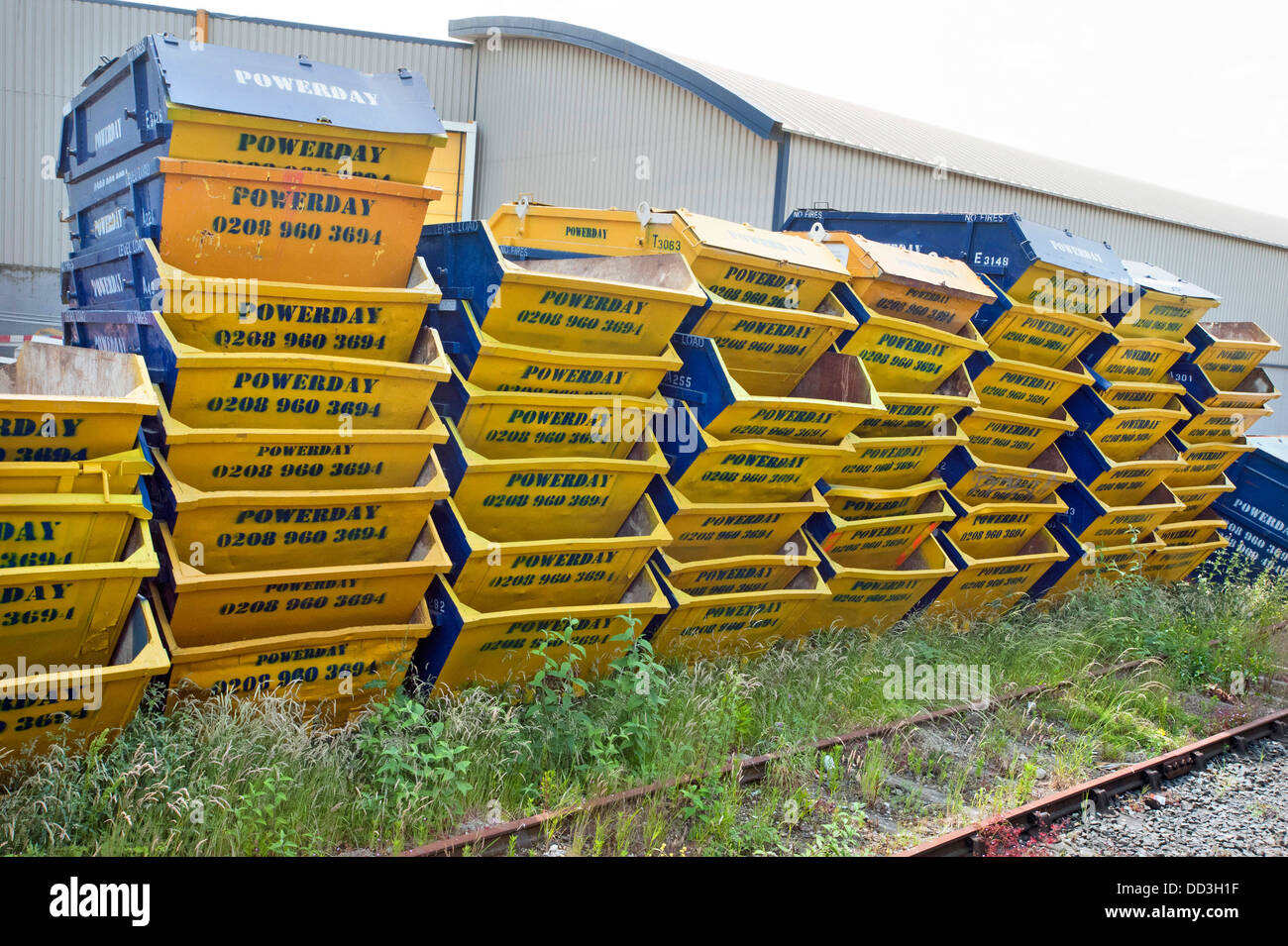 Stapel von stapelten sich gelb und blau Müll "Powerday" überspringt, einige acht tiefen stand in einem Recyclinghof durch eine Eisenbahnlinie in Willesden, Nord-London Stockfoto