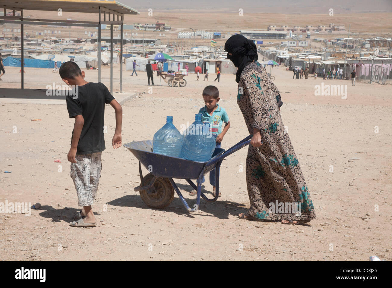 Domiz Flüchtlingslager, Duhok, Irak. 25. August 2013. Eine Frau, die Wasser in ihr Zelt mit ihren Söhnen. Das Hauptproblem von Domiz Flüchtlinge Camp, das 100.000 Menschen beherbergt, ist der Mangel an Wasser. Die Temperatur während des Tages ist bis zu 45° C Credit: Francesco Gustincich/Alamy Live News Stockfoto