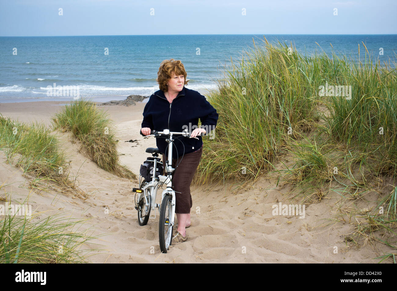 Eine Frau mit ihrem Fahrrad In den Sand am Wasser entlang; Northumberland, England Stockfoto