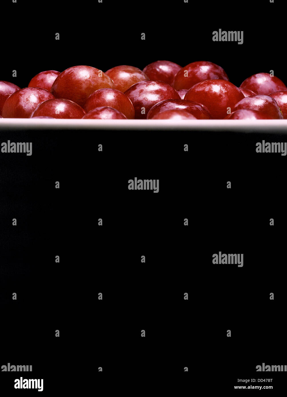 Rote Trauben in eine Schüssel geben. Dramatische Beleuchtung und interessante vertikale Zusammensetzung. Stockfoto