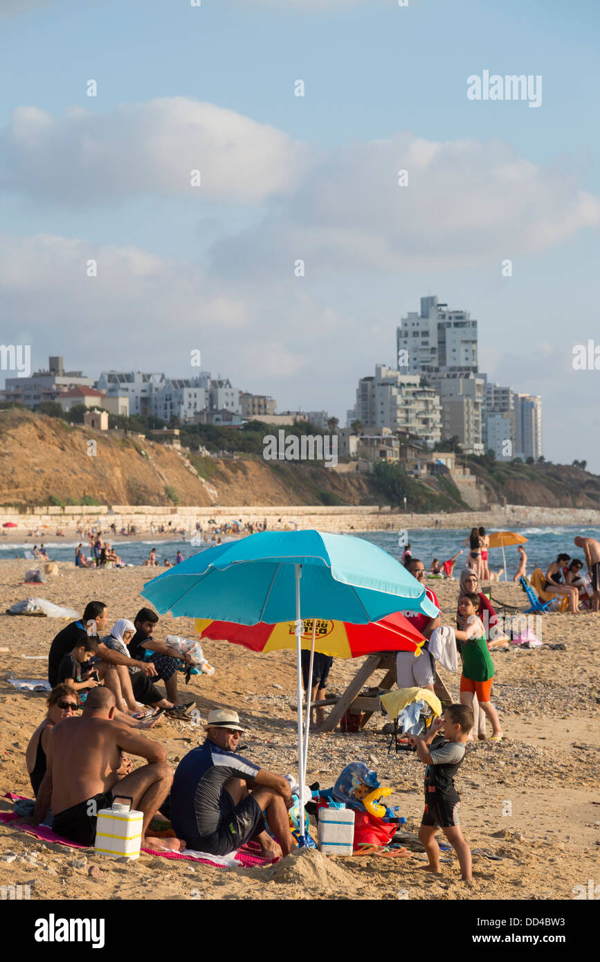 Familie entspannend am Strand mit hohen steigenden Gehäuse Buildibg im Hintergrund. Givat Alyah Strand. Jaffa. Israel. Stockfoto