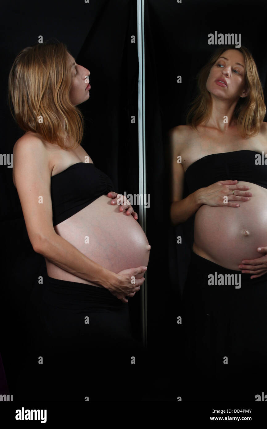 Schwangere Frau schaut sich im Spiegel Stockfoto