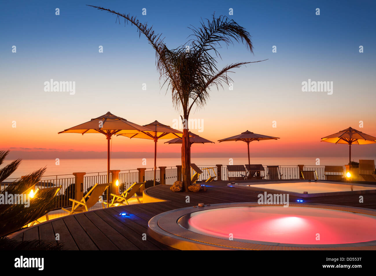 Sommerzeit: schöne Aussicht auf rote Morgendämmerung am Pool mit Palmen und Sonnenschirmen an Stockfoto