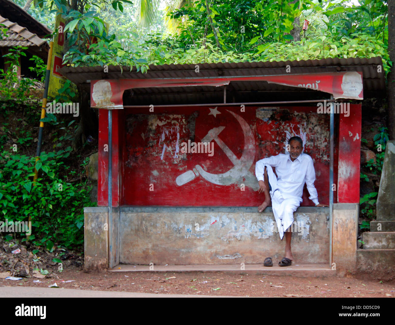 Mann sitzt auf einem Schuppen mit kommunistischen Graffiti; ländliche Kerala, Indien Stockfoto