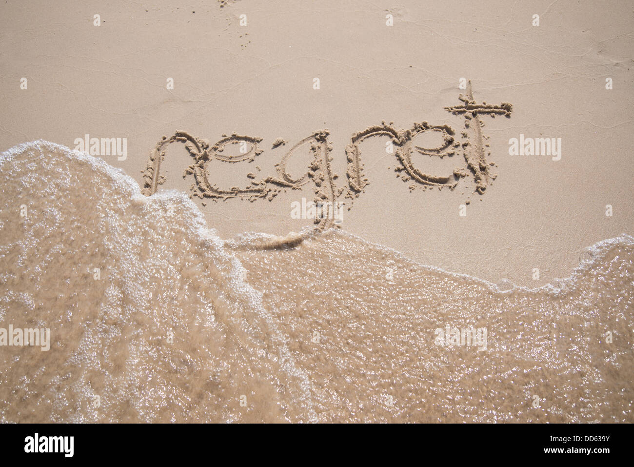 Das Wort "Bedauern", geschrieben in den Sand, die von einer Welle weggespült. Stockfoto