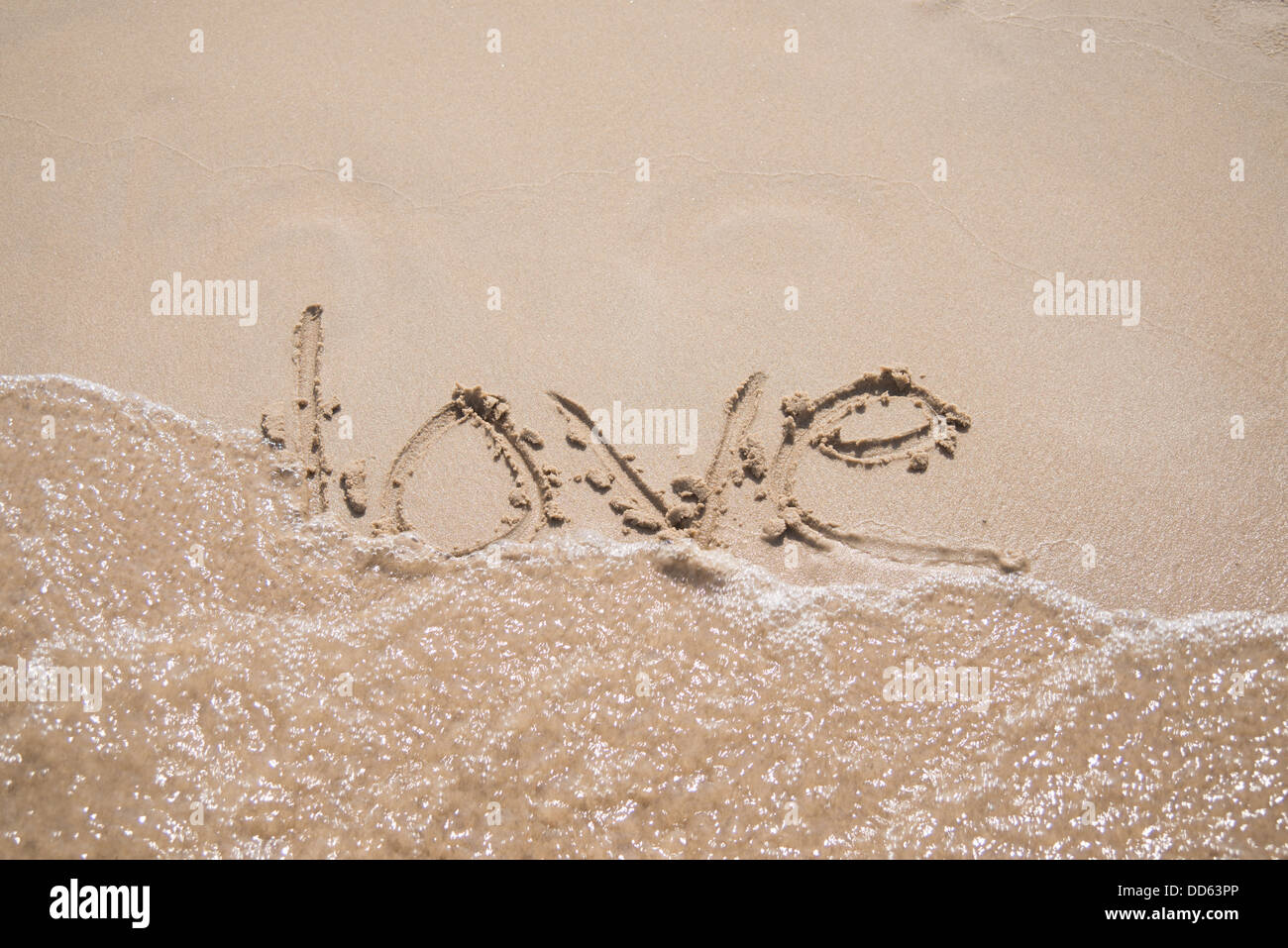 Das Wort "Liebe" in den Sand, von einer Welle weggespült geschrieben. Stockfoto
