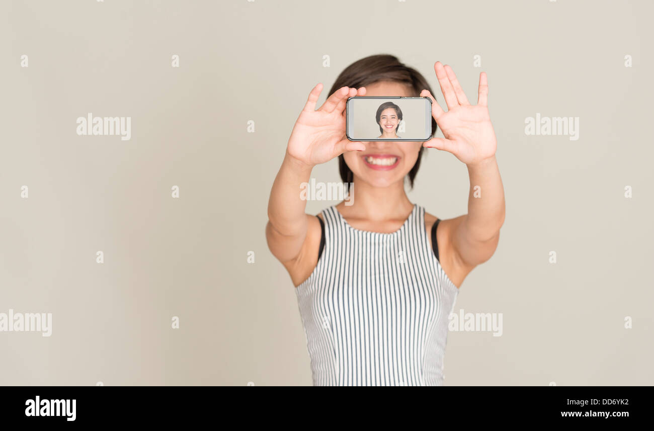 Junge Frau Lächeln und nehmen Sie ein Bild von sich selbst mit der Kamera in einem Handy Stockfoto
