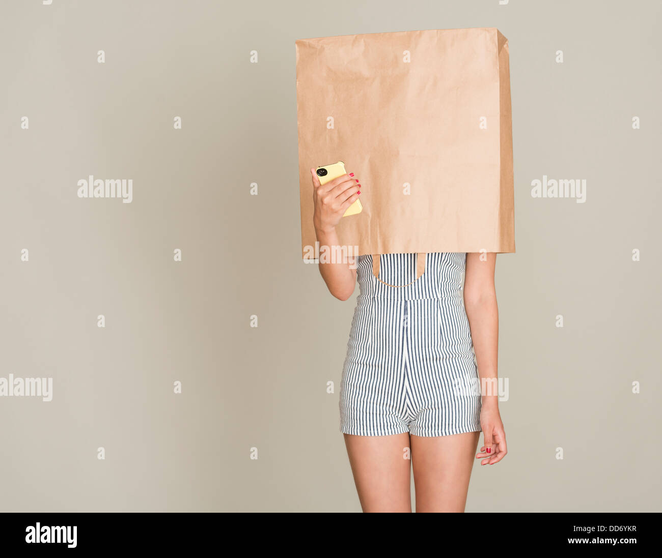 Anonymer Anrufer. Junge Frau mit Papiertüte über den Kopf halten eines Handys. Stockfoto