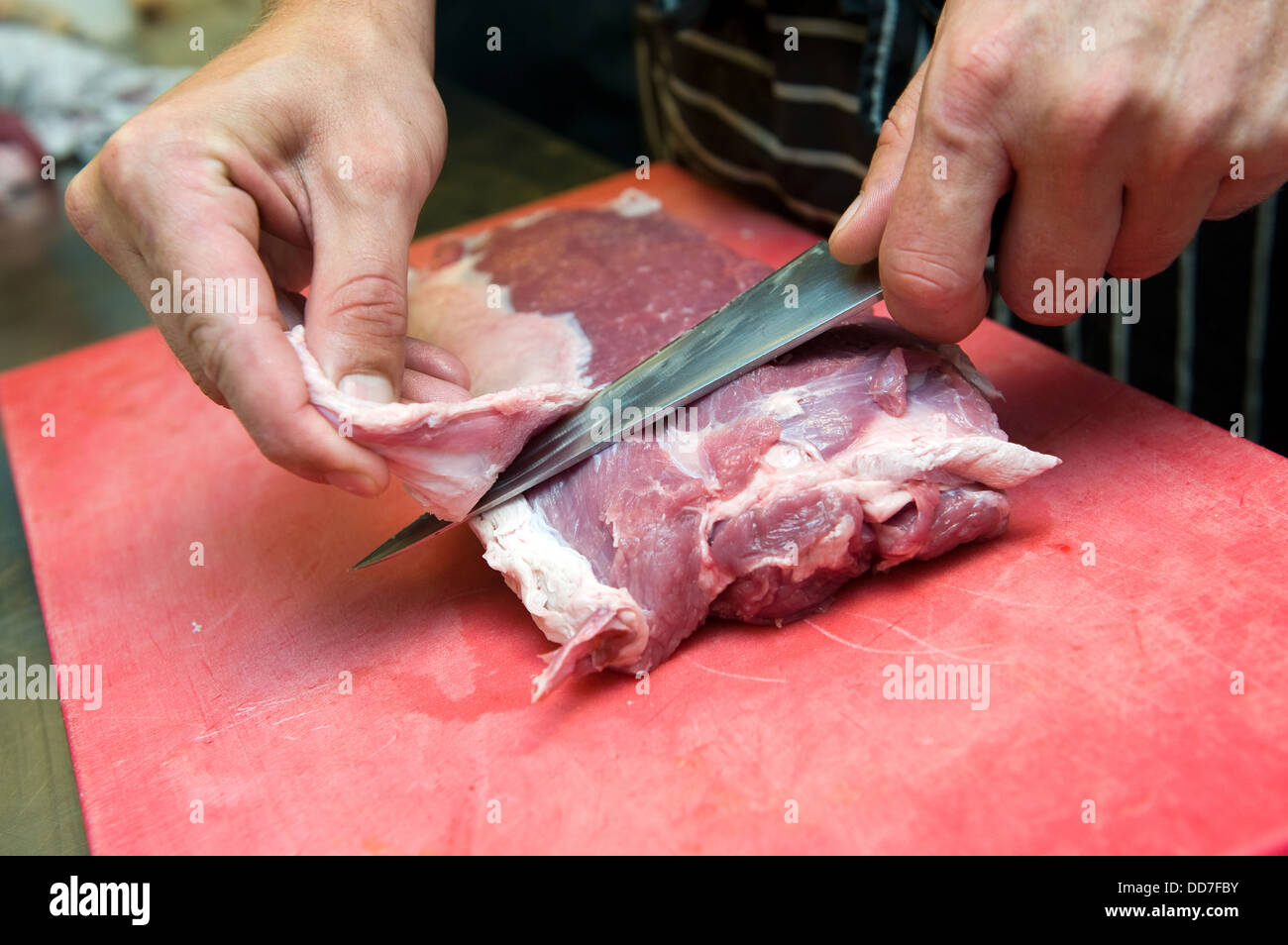 Ein Koch in der Küche arbeitet mit einem Messer an einem Stück Fleisch Stockfoto