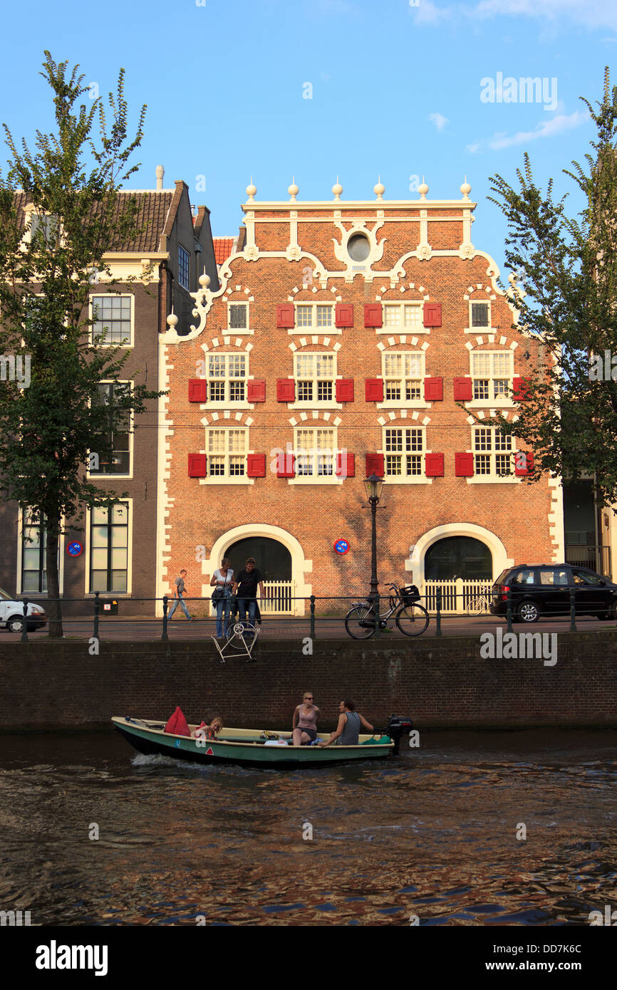 Ikonische niederländische Gebäude in der Dämmerung mit Menschen neben dem Kanal Bootstouren und sightseeing in Amsterdam. Stockfoto