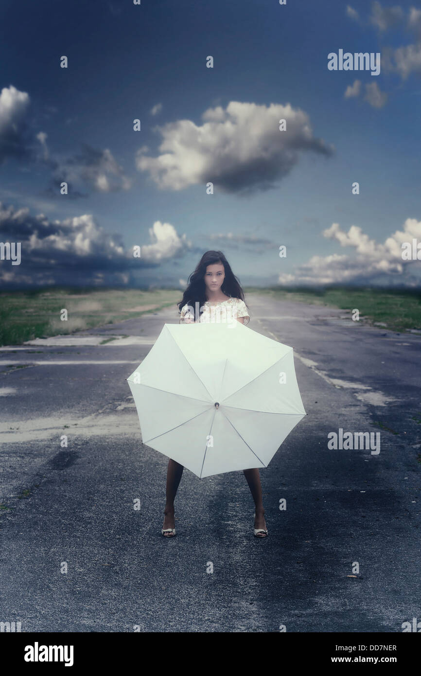 ein Mädchen in einem geblümten Kleid auf einer Straße mit einem weißen Schirm Stockfoto