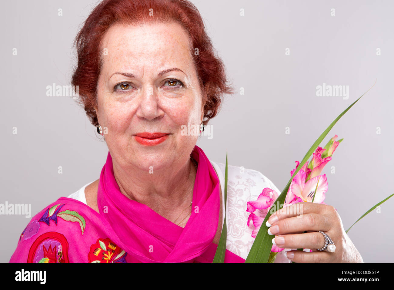 Red Hair Senior Woman mit Gladiolen Blume suchen bestimmt. Stockfoto