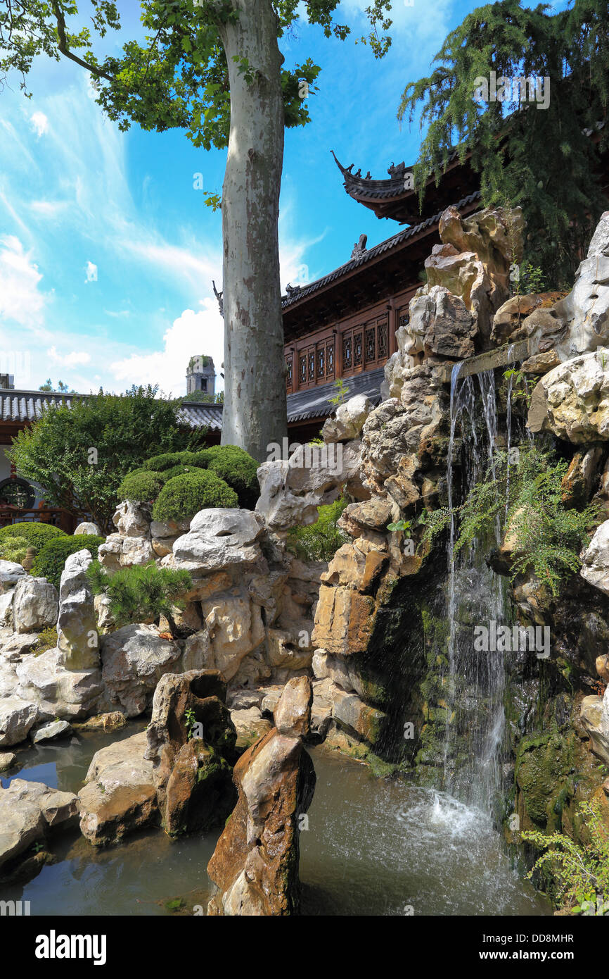 Chinesischer Tempel in einem schönen Garten mit einem Wasserfall, Bäumen und Steinen. blauer Himmel. Niemand Stockfoto