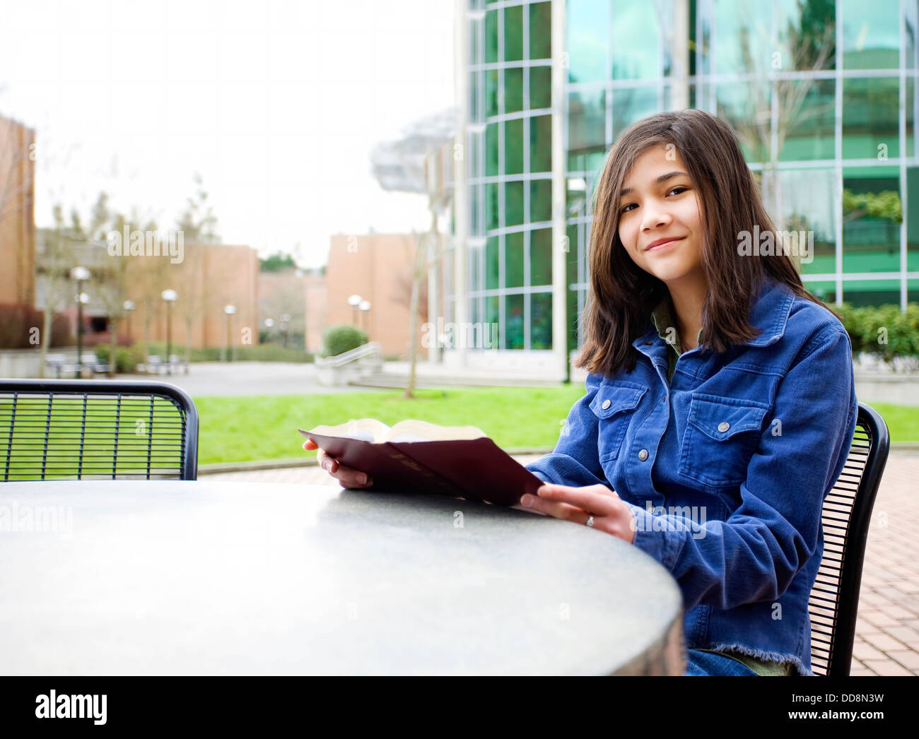 Zwölf Jahre alten biracial Mädchen sitzen im Freien ein Buch zu lesen Stockfoto