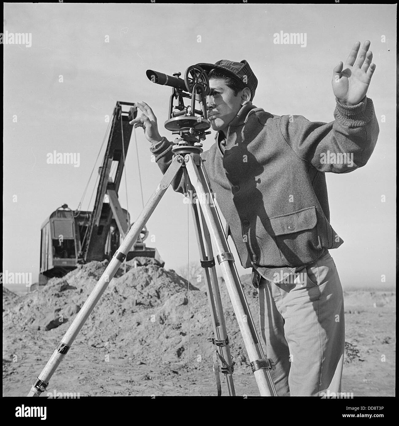 Dieses Bild zeigt eine junge Nisei (japanische Amerikanerin der zweiten Generation), die ein Vermessungsinstrument im Granada Relocation Center (Amache) in Colorado betreibt und die Rolle der Internierten in den täglichen Operationen des Lagers widerspiegelt. Stockfoto