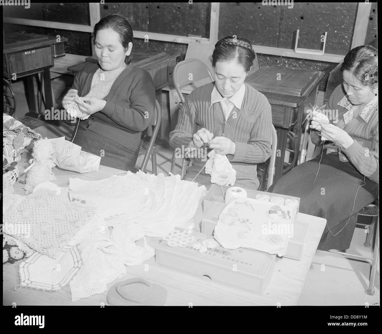 Dieses Bild zeigt drei Mitglieder einer Häkelklasse für Erwachsene im Granada Relocation Center, auch bekannt als Amache Internierungslager in Colorado. Das Lager beherbergte japanische Amerikaner während des Zweiten Weltkriegs Stockfoto