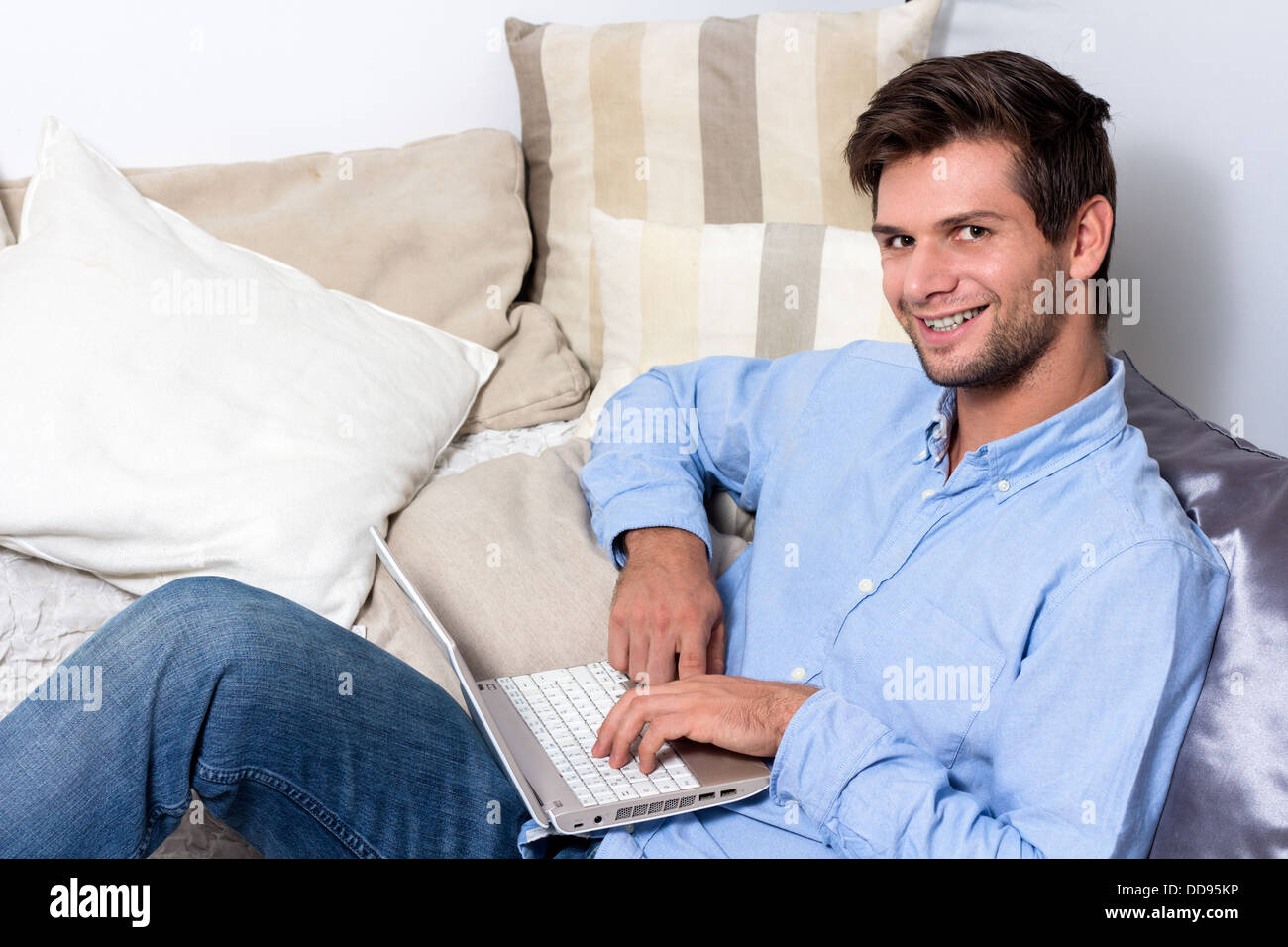 Junge Brünette Mann im blauen Hemd mit Laptop auf couch Stockfoto
