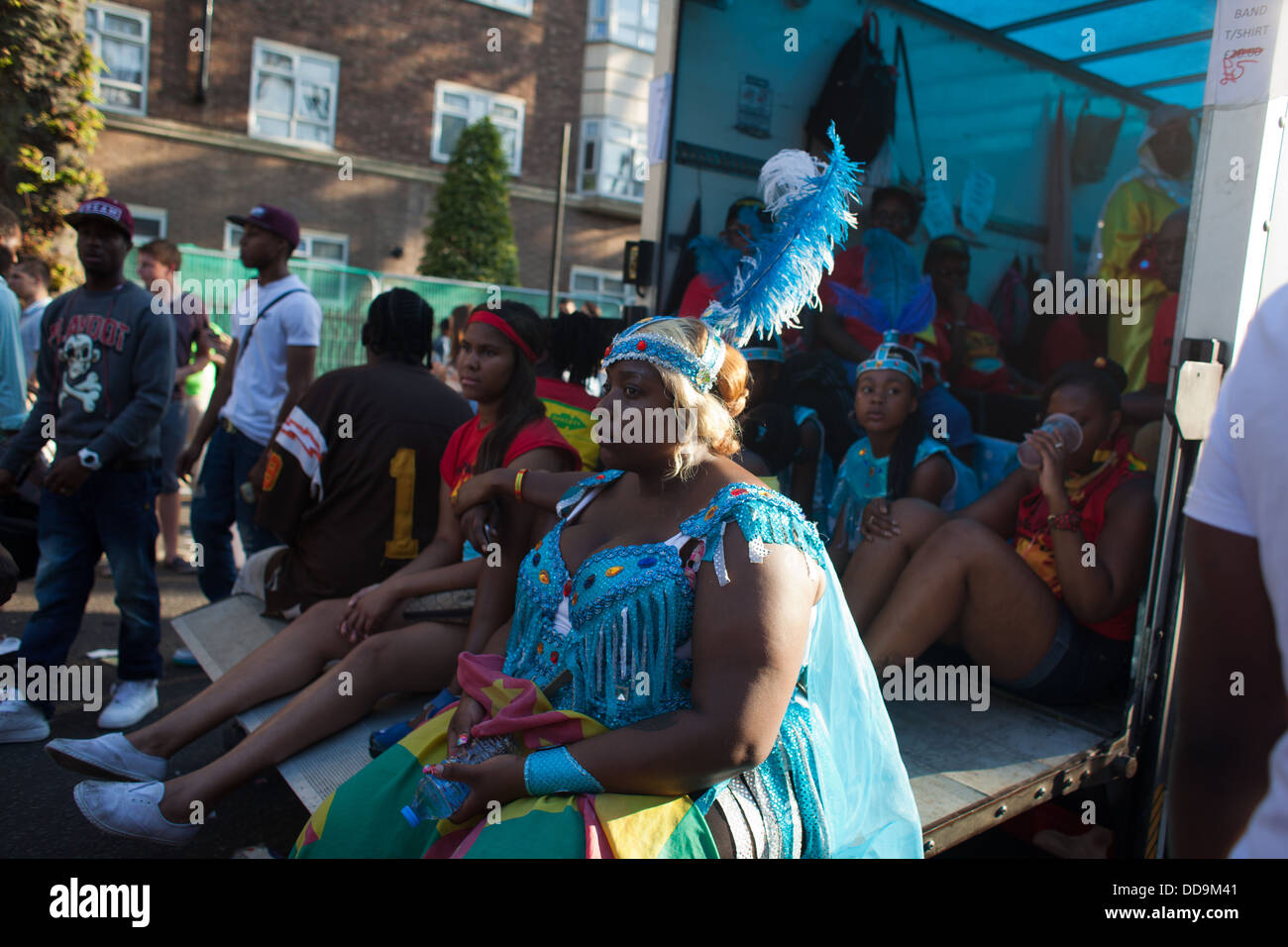 Ein schwarzes Mädchen, gekleidet in blaue Federn und Kostüm Rest auf der Ladefläche eines Lastwagens Karneval mit ihren Freunden nach zwei Tagen des Tanzes Stockfoto