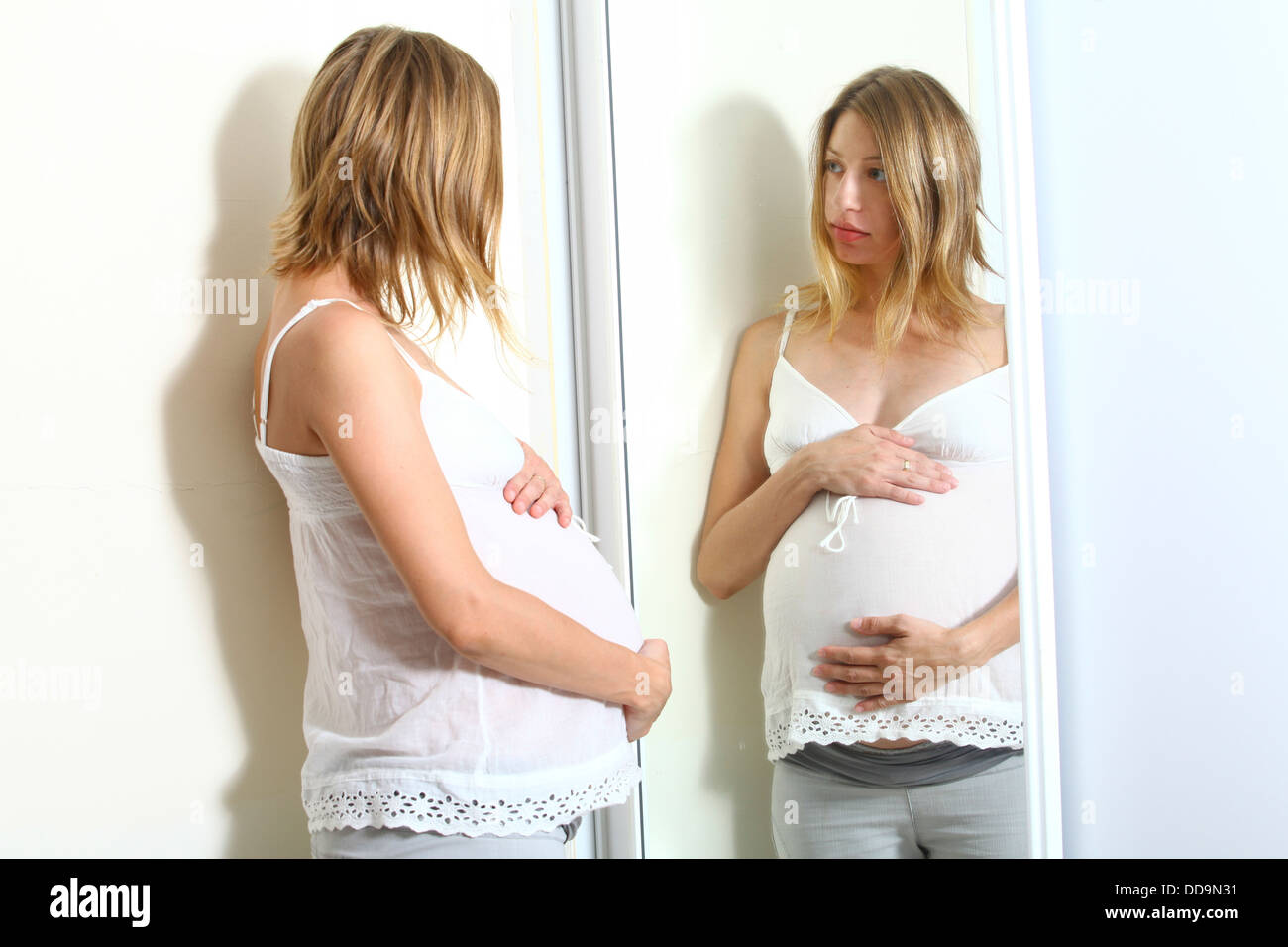 Schwangere Frau schaut ihre Reflexion in einem Spiegel Modell Release verfügbar Stockfoto