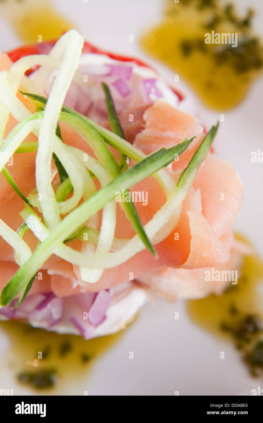 Gourmet-Teller geräucherten Lachs auf Käse, Avocado, rote Zwiebel und beträufelt mit Basilikum-Pesto, garniert mit Gurken-Streifen. Stockfoto