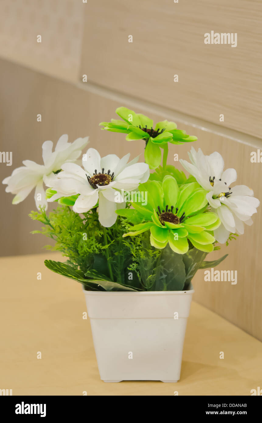 Plastikblumen in weißer Vase auf Holztisch Stockfoto