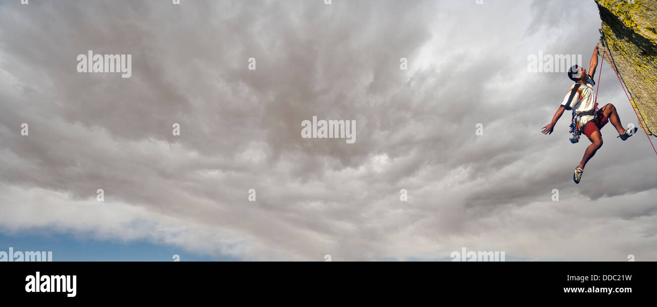 Rock Climber Kämpfe bis zum Gipfel des einen herausfordernden Höhepunkt als Gewitterwolken bauen hinter ihm. Stockfoto