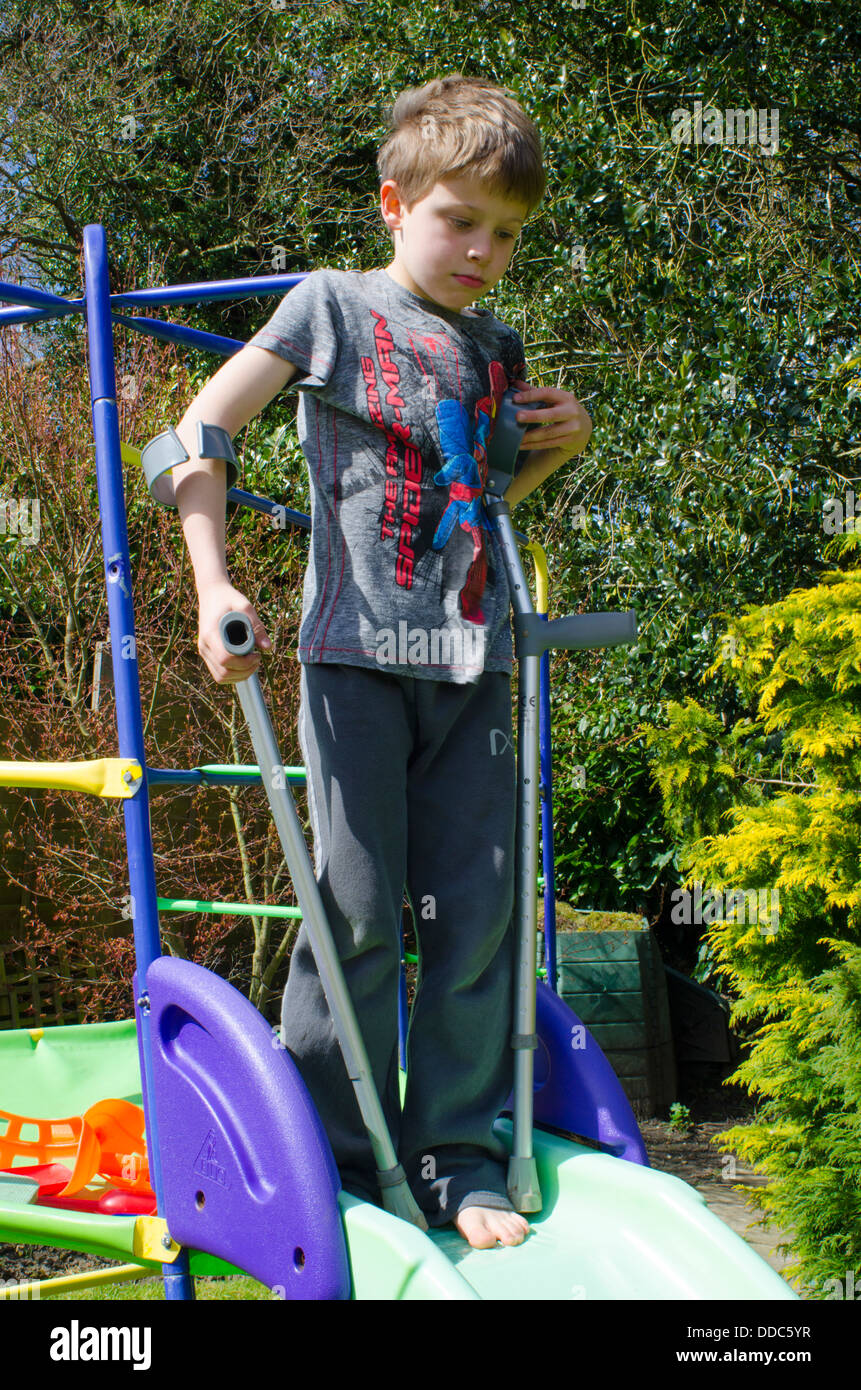 acht Jahre alter Junge mit Krücken als abenteuerlich auf einem Garten Folie darüber nachzudenken. Stockfoto