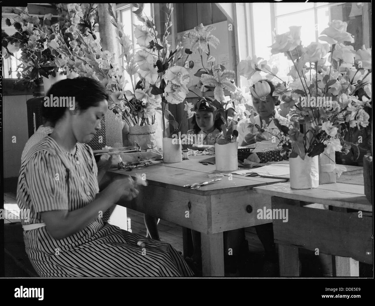 Dieses Bild zeigt Einzelpersonen, die künstliche Blumen in der Kunstschule im Manzanar Relocation Center herstellen, einem Internierungslager für japanische Amerikaner aus dem Zweiten Weltkrieg in Kalifornien. Stockfoto