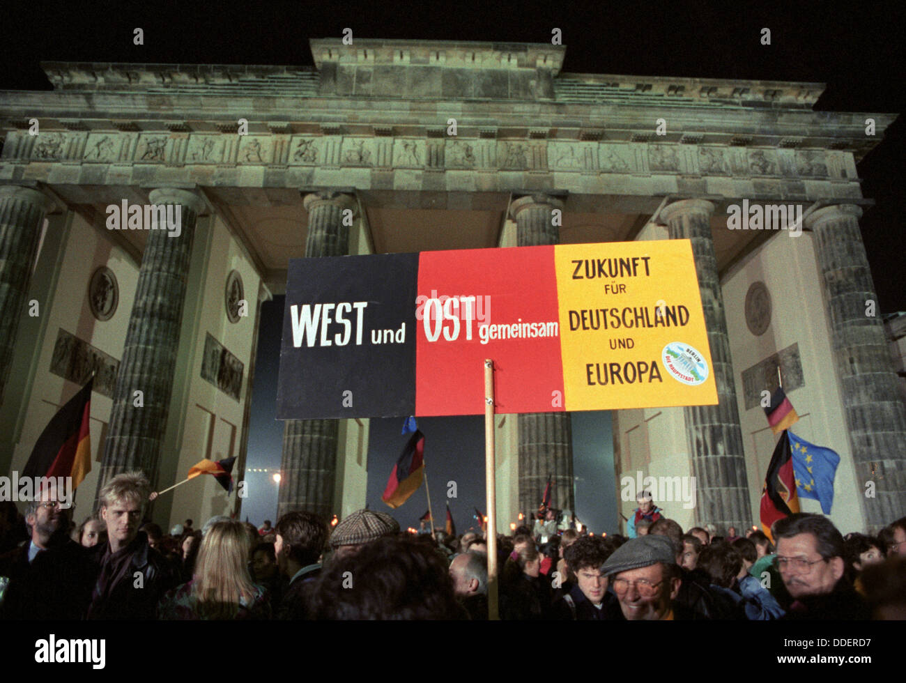Ein Poster mit dem print "Westen und Osten - Zukunft für Deutschland und Europa" ist vor dem Brandenburger Tor in Berlin in der Nacht zum 3. Oktober 1990 statt. Mit dem Beitritt der DDR zur Bundesrepublik Deutschland sind die deutschen schließlich in einen souveränen Staat 45 Jahre nach dem Ende des zweiten Weltkriegs wieder vereint. Stockfoto