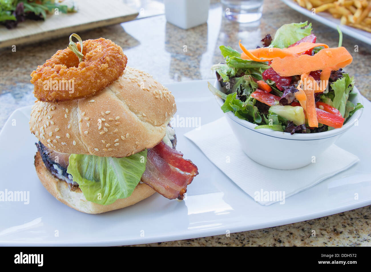Hamburger mit Zwiebel Ring Schinken Rindfleisch Patty Salat und Schale von Bio-Gemüse-Salat Stockfoto