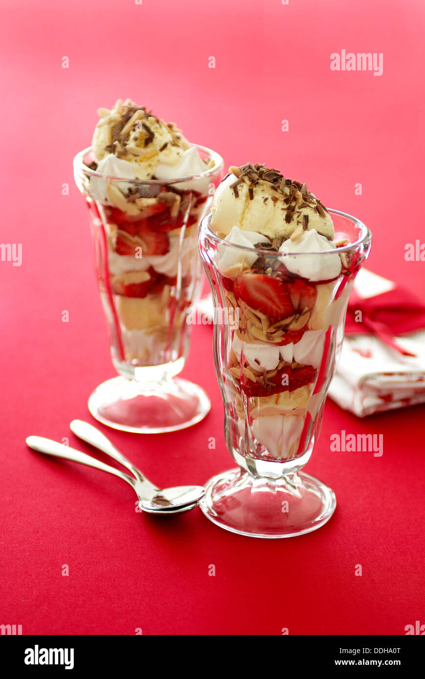 Zwei Erdbeer Eisbecher mit Baiser, Sahne, Eis und Schokolade auf einem roten Tischfläche. Stockfoto