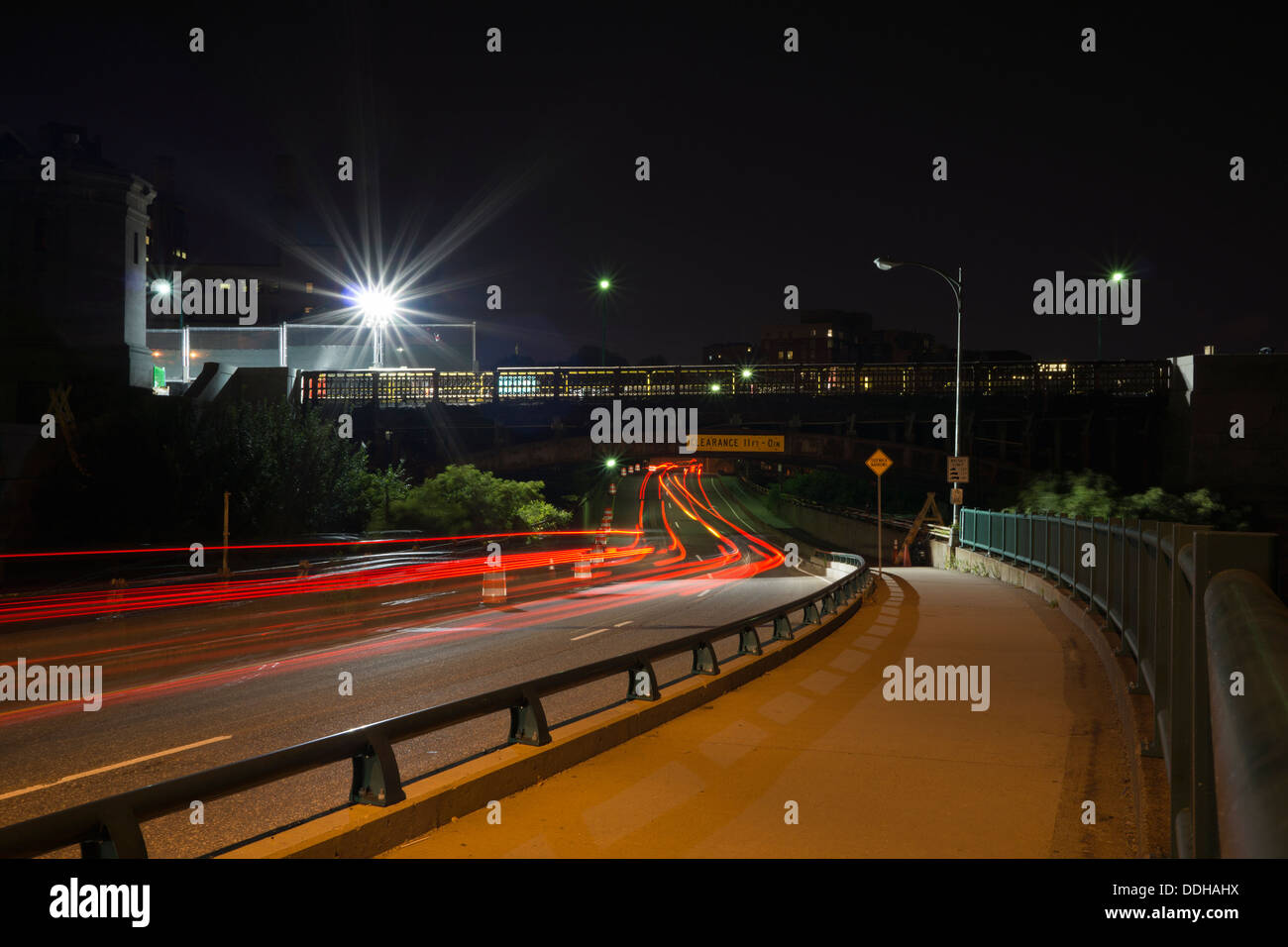 Verlassener Bürgersteig und verschwommene Autolichter, die nachts unter der Brücke entlang des Memorial Drive, einer Straße in Boston, Mass, hindurchfahren Stockfoto