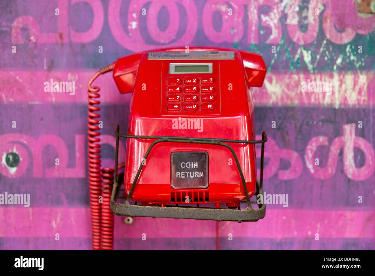 Alte rote Telefon gegen eine Wand mit rosa Malayalam-Skript Stockfoto