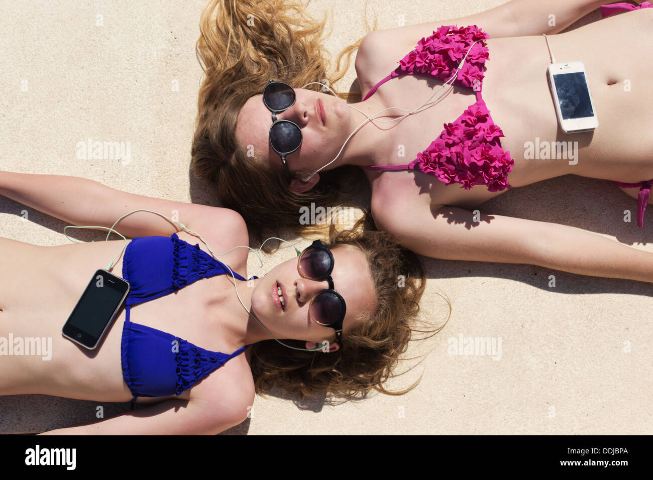 Zwei Mädchen im Teenageralter liegen in der Sonne, die Musik auf ihrem Handy anhören. Stockfoto