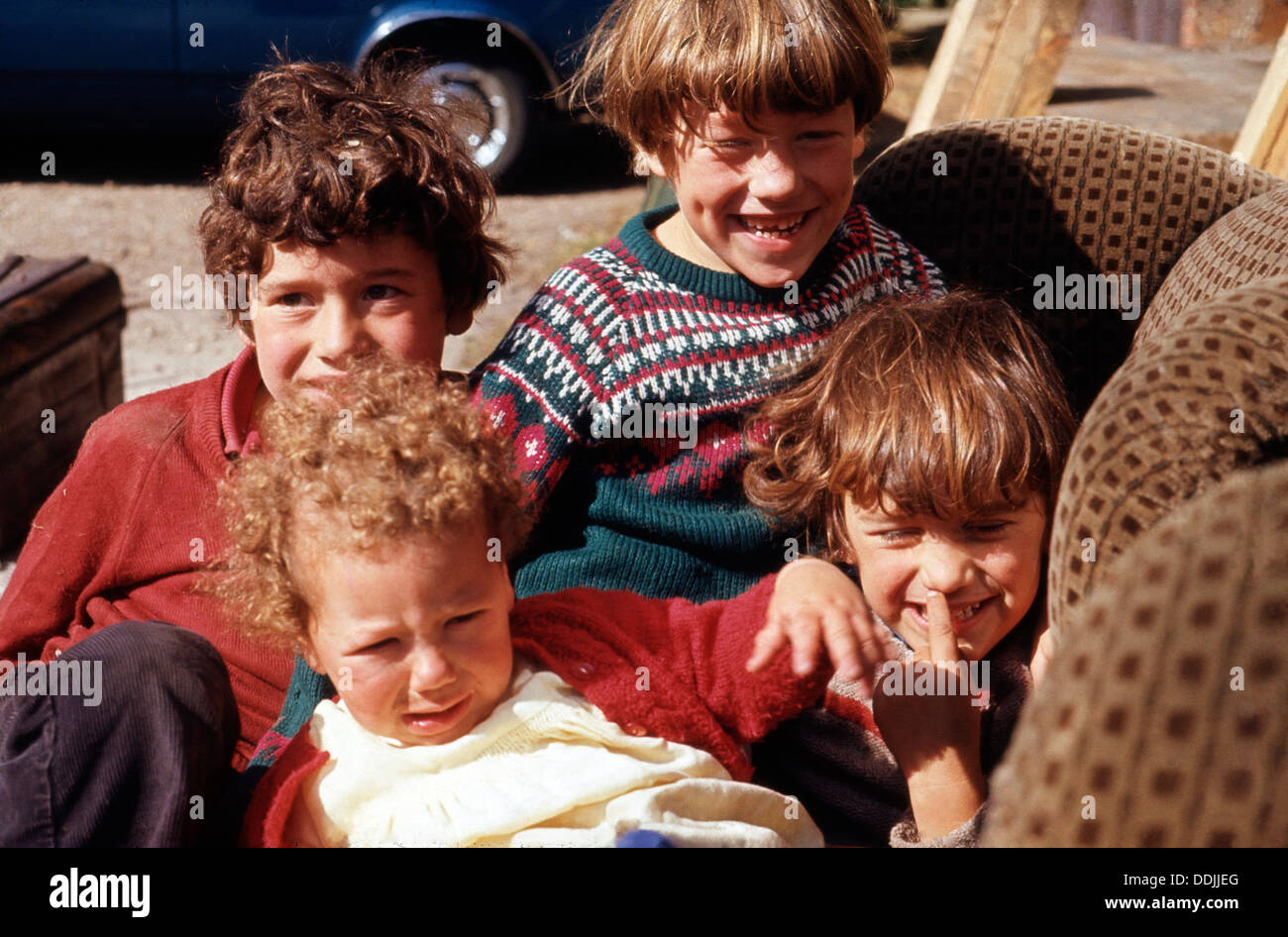 Brüder und Schwesternjungen Mädchen spielen draußen auf einem alten gepolsterten Stuhl Norwich, Norfolk, England Großbritannien England in den 1970er Jahren 1973 KATHY DEWITT Stockfoto