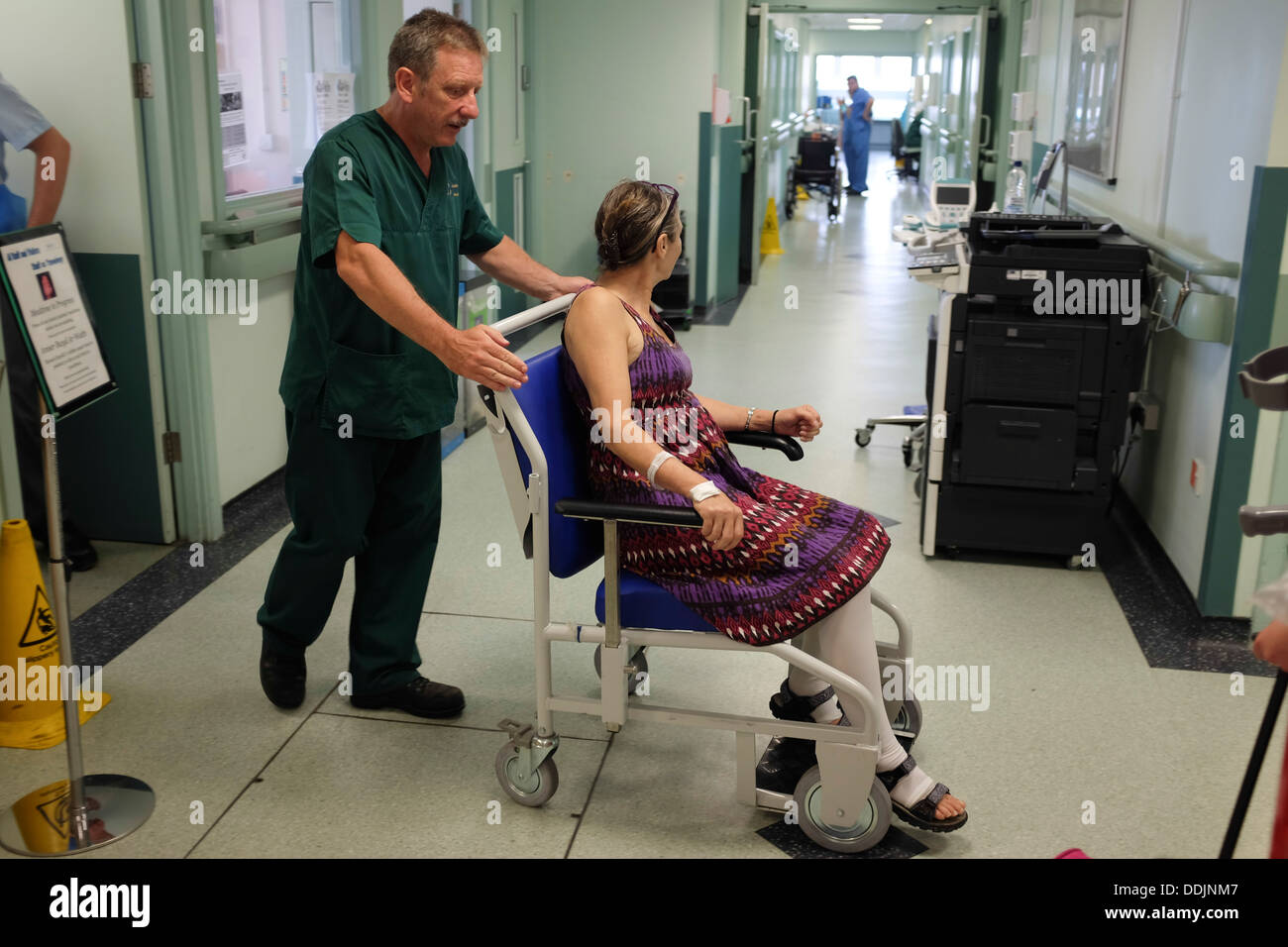 Ein Krankenhaus-Träger helfen, eine Frau der Entlassung aus dem NHS Krankenhaus im Rollstuhl nach einer Hüft-Operation UK Stockfoto