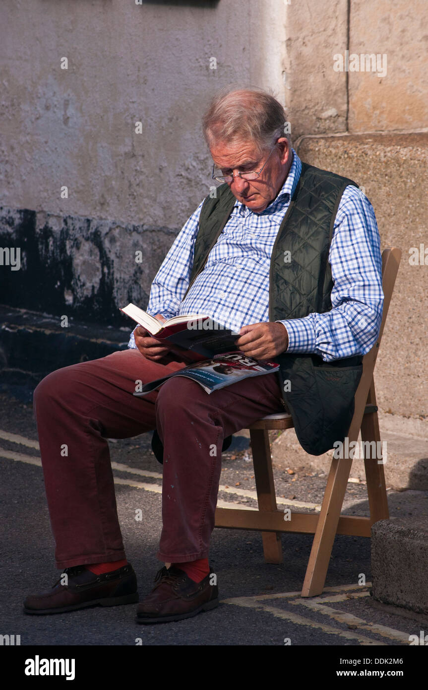 Alter Mann Buch sitzen draußen auf der Straße Stockfoto
