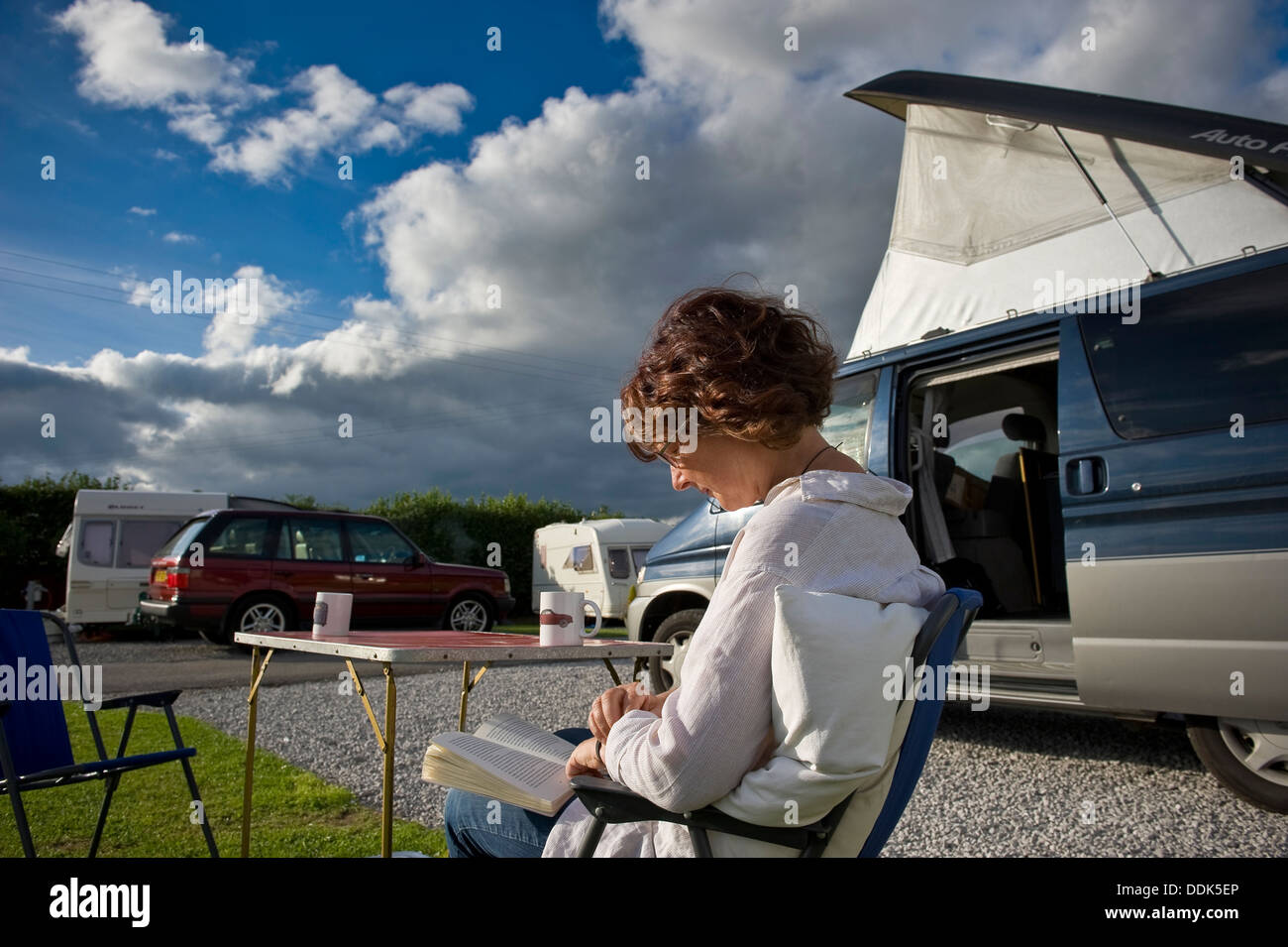 Frau liest ein Buch neben ihrem Wohnmobil auf einem Campingplatz in Cheshire, Großbritannien Stockfoto